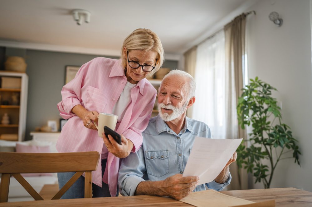 Senior,Couple,Read,A,Document,From,Envelope,And,Use,Cellphone